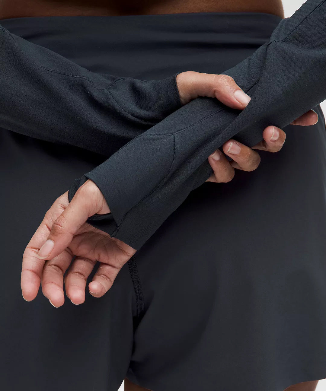 Close-up of a woman’s hands wearing a black performance long sleeve with thumb holes and athletic black shorts, designed for active comfort and gym-ready mobility.