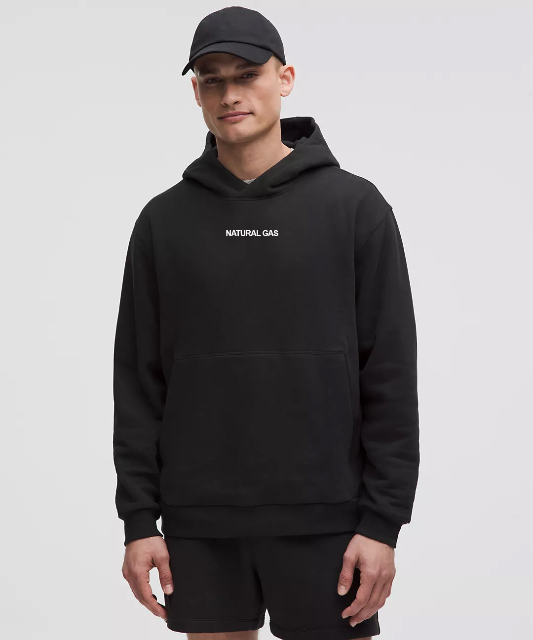 A male model wearing a black hoodie with 'NATURAL GAS' embroidered in white text on the center chest, paired with a black cap.