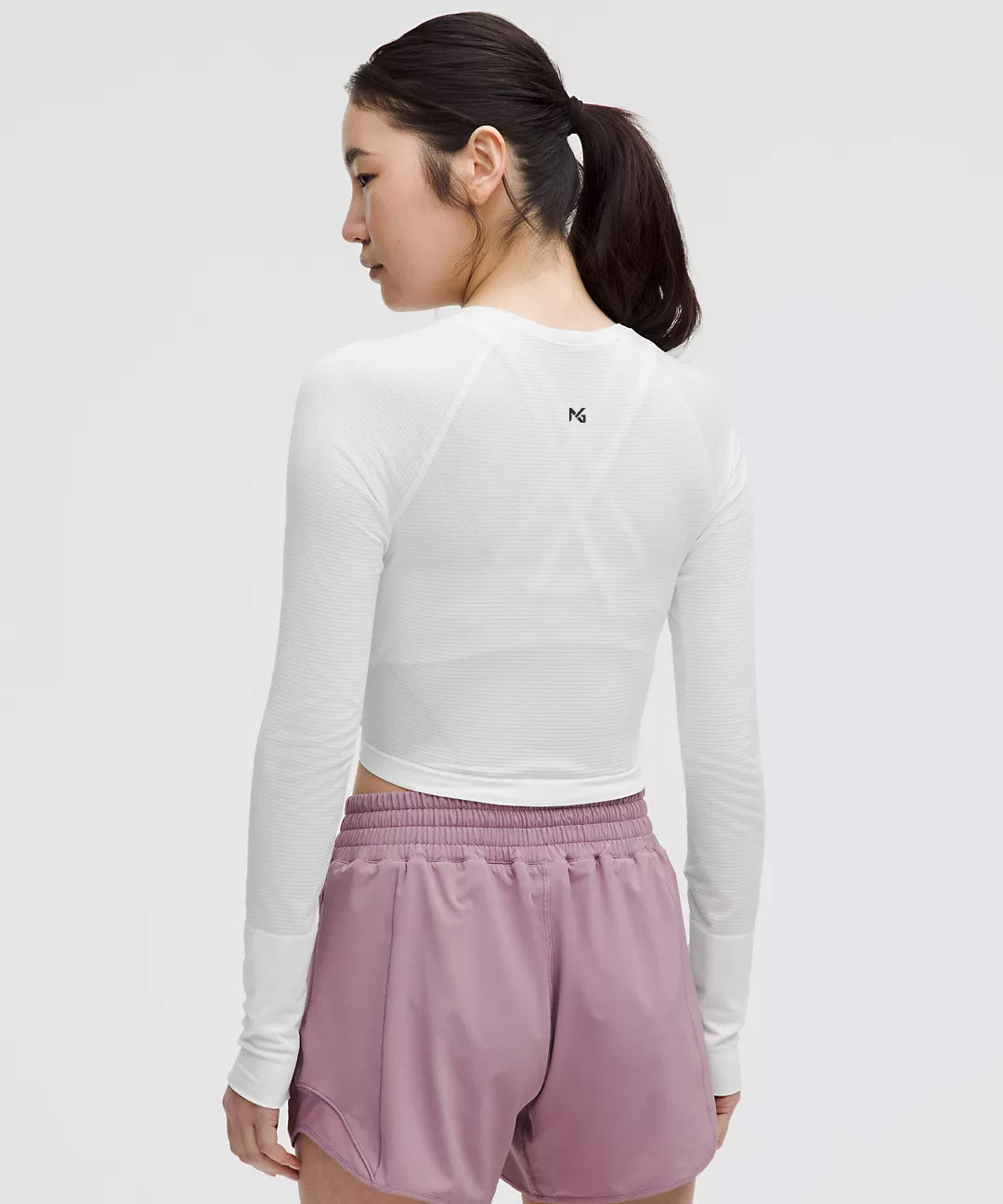 Back View of Women’s White Long Sleeve Crop Top – Natural Gas Logo Between Shoulder Blades – Lightweight Fitted Athletic Shirt with Lilac Workout Shorts