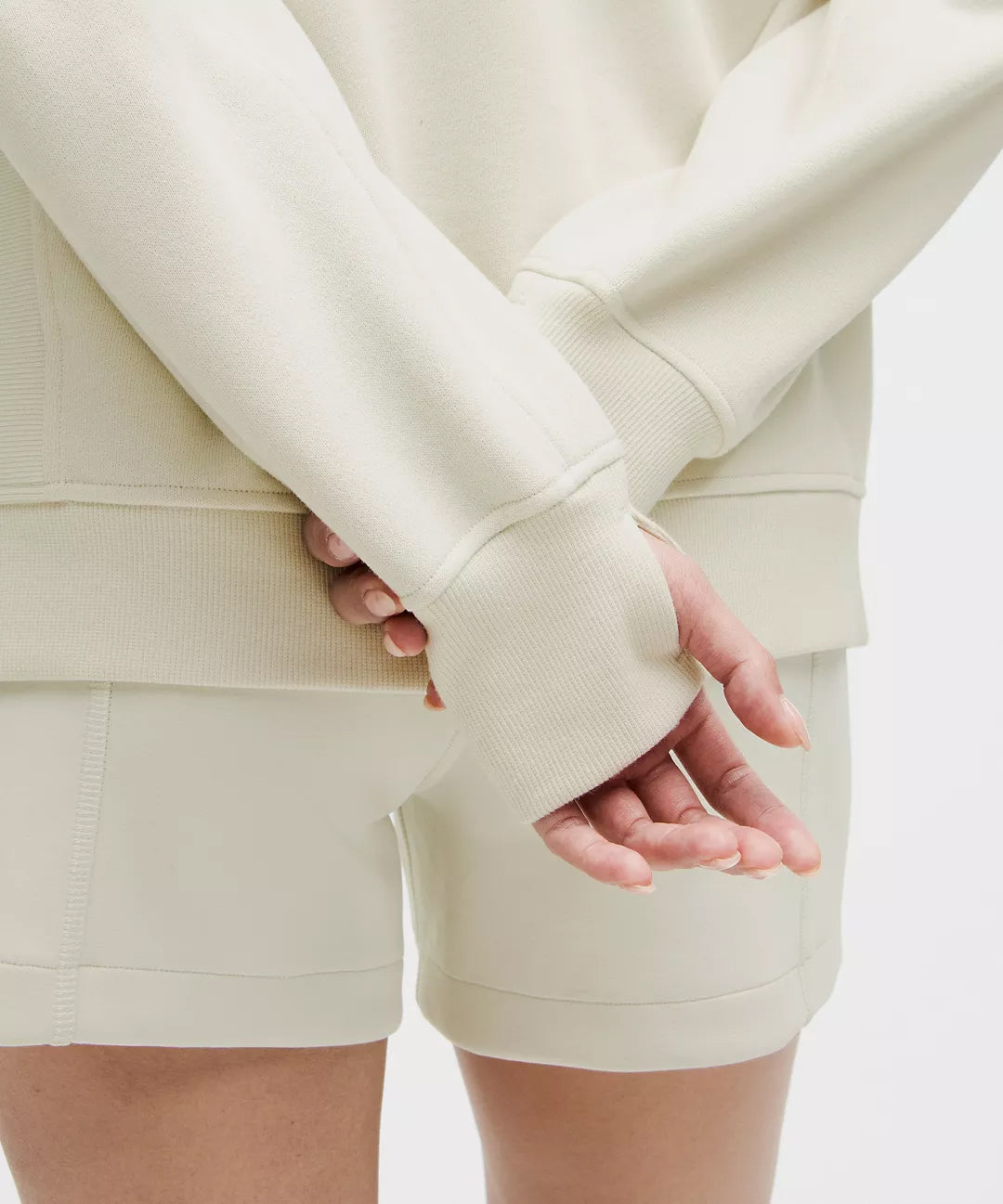 Close-Up of Woman Wearing Off-White Natural Gas Hoodie and Shorts – Thumbhole Sleeve Detail and Soft Ribbed Fabric – Minimalist Activewear Set