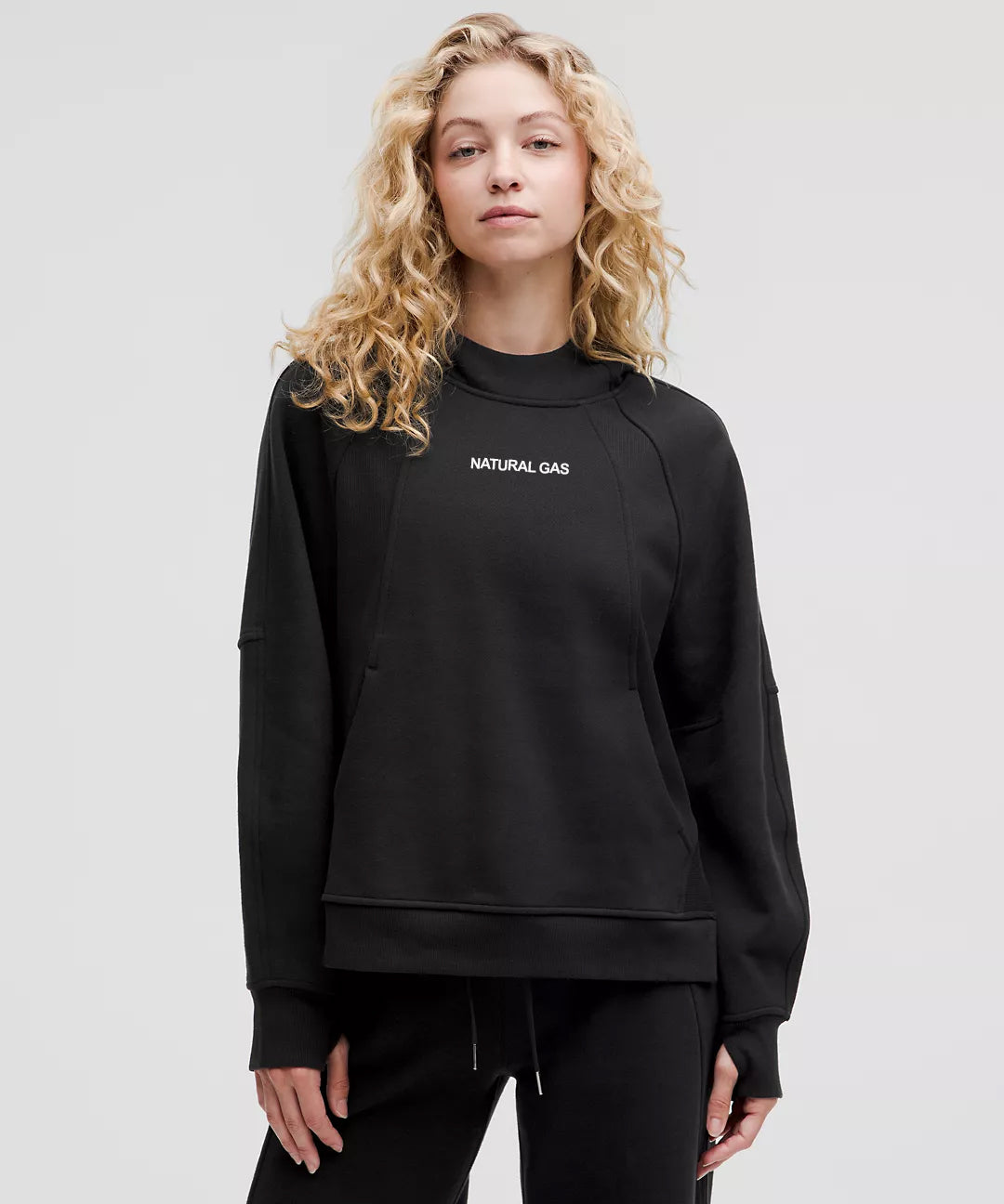 Woman wearing Natural Gas black hoodie with minimalist white logo, featuring relaxed athletic fit and ribbed cuffs for everyday comfort and style.