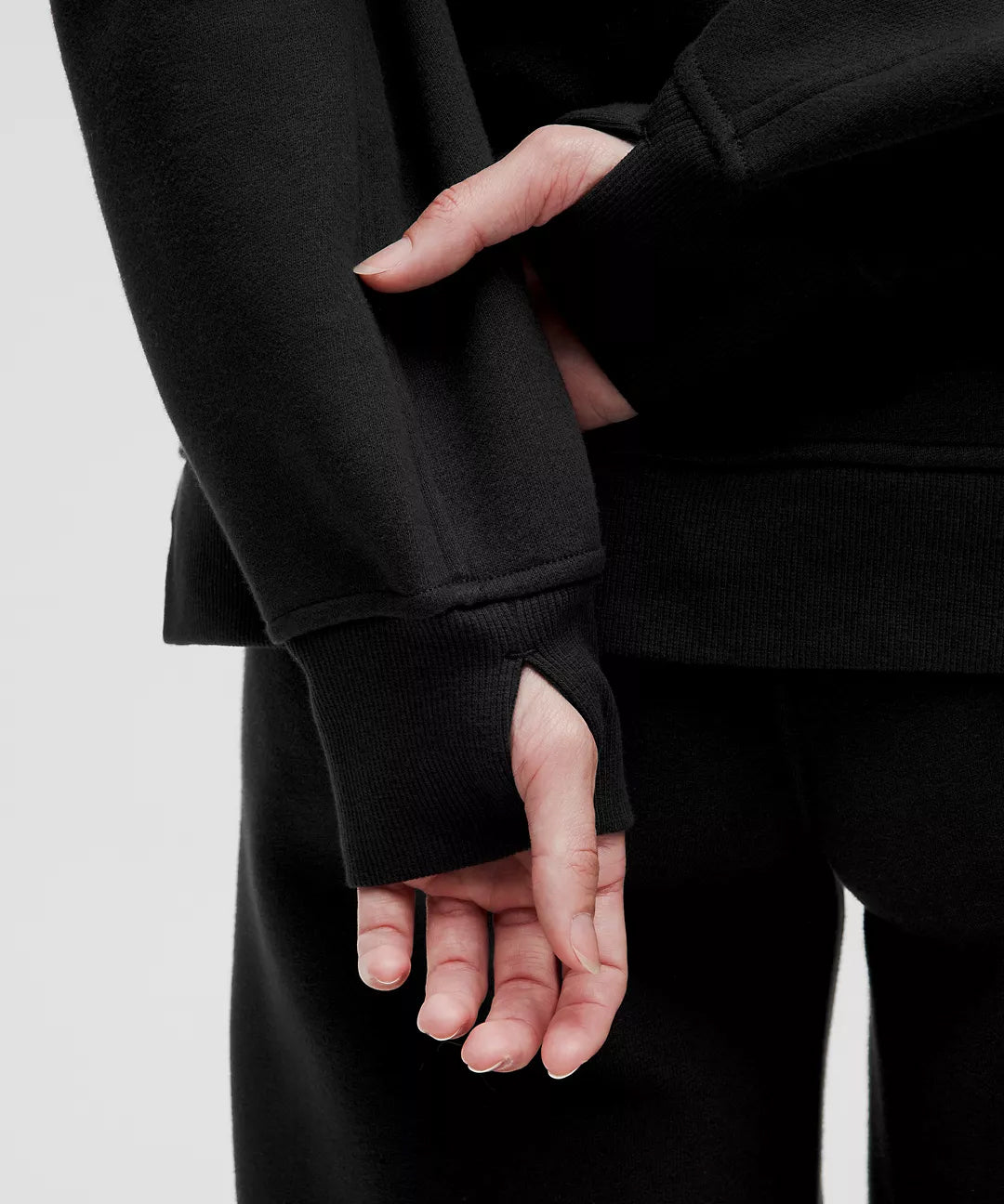 Closeup of woman’s hand in thumbhole sleeve of black hoodie, showcasing Natural Gas minimalist athleticwear with premium stitching and comfort-focused design.