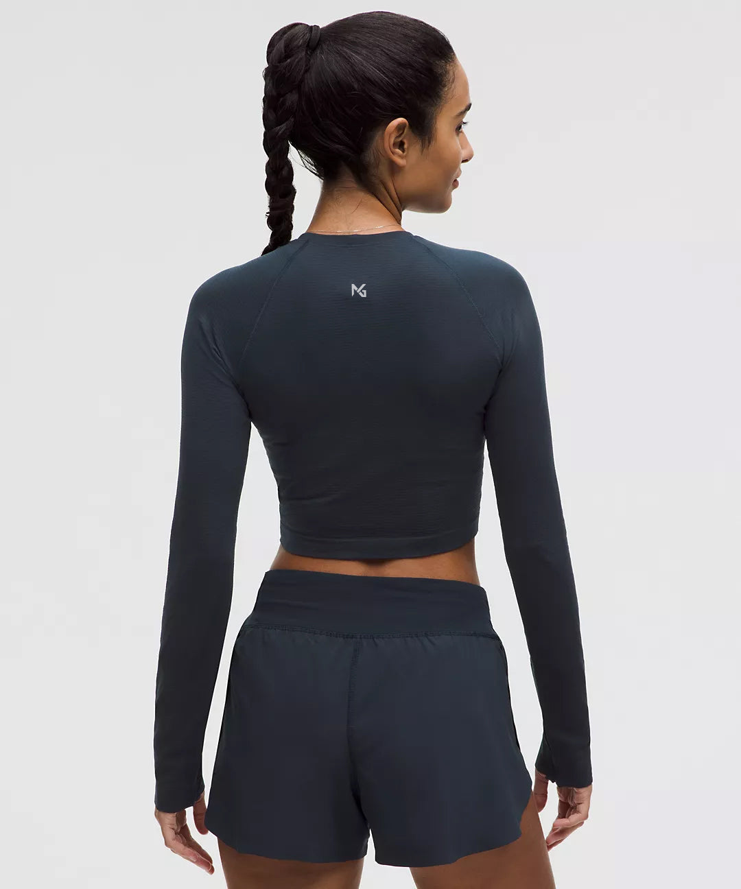 Back view of woman wearing a black long sleeve crop top and athletic shorts, featuring the Natural Gas logo on the upper back; ideal for showcasing minimalist gym apparel.